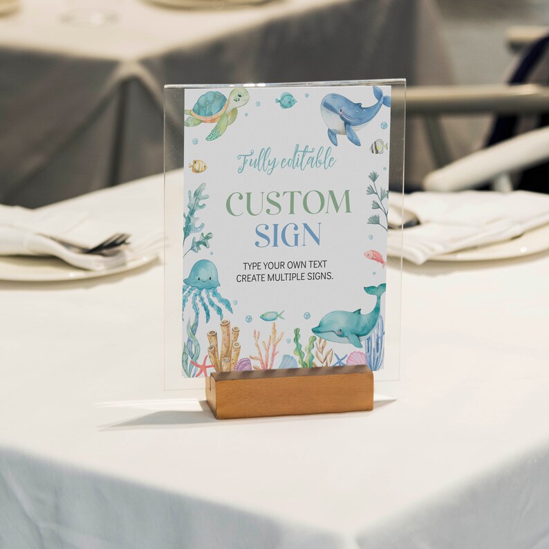 May include: A customizable sign with a watercolor design of sea creatures, including a turtle, a whale, a jellyfish, and a dolphin. The sign is on a wooden stand and says "Fully editable CUSTOM SIGN TYPE YOUR OWN TEXT CREATE MULTIPLE SIGNS."