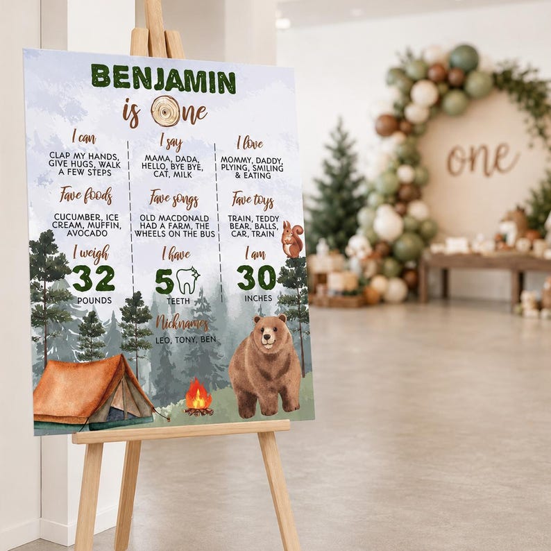 May include: A rectangular milestone birthday sign featuring a forest theme with a brown bear, a tent, and a campfire. The text reads Benjamin is one, listing milestones like 32 pounds, 5 teeth, and 30 inches, alongside favorite foods, songs, and toys.