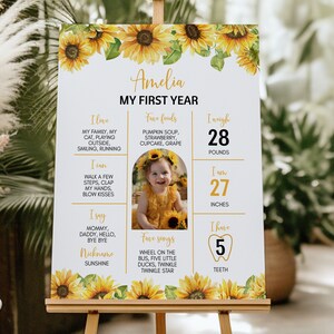 May include: A white poster with a sunflower border and a photo of a baby girl. The poster is titled "Amelia My First Year" and includes details about the baby's age, weight, height, and favorite things. The poster is perfect for a first birthday party.