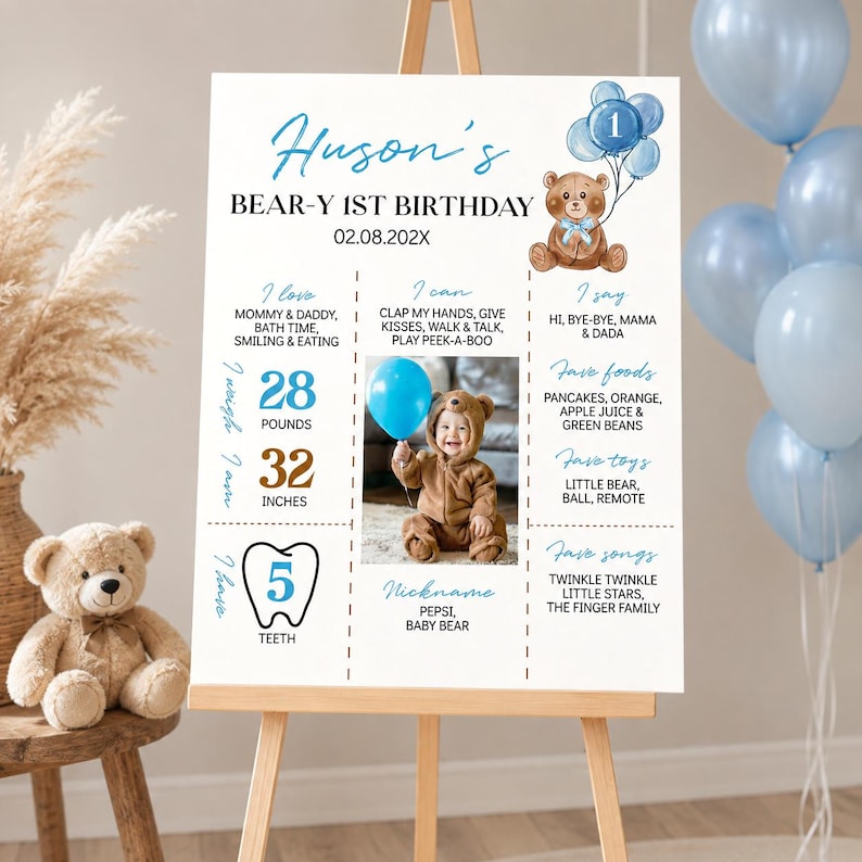 May include: A white birthday milestone sign for Huson's 1st birthday featuring a brown teddy bear illustration, blue balloons, and text detailing baby milestones, including 28 pounds and 32 inches, with a central photo of a child in a bear suit.