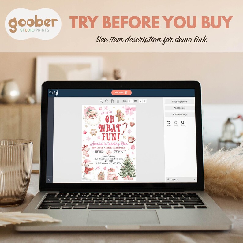 May include: A laptop displays a Christmas-themed invitation design with Santa Claus, gingerbread men, and a Christmas tree. The text on the invitation reads "OH WHAT FUN!" and "Amelia is turning One." The laptop is open on a table with the text "TRY BEFORE YOU BUY".