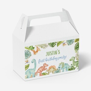 May include: A white cardboard gable box featuring a colorful watercolor illustration of various dinosaurs and tropical leaves. The text on the front reads Justin's first birthday party! in green and blue script and block lettering.
