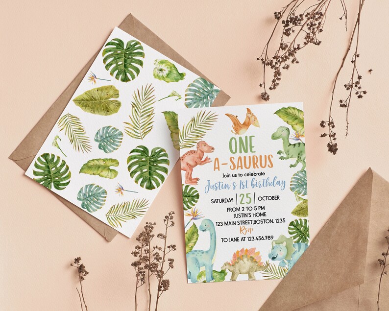 Op de afbeelding: Een verjaardagsuitnodigingskaart en een bijpassende envelopvoering met aquarelillustraties van diverse groene tropische bladeren en kleurrijke dinosaurussen. De tekst luidt ONE A-SAURUS, join us to celebrate Justin's 1st birthday, Saturday 25 October.