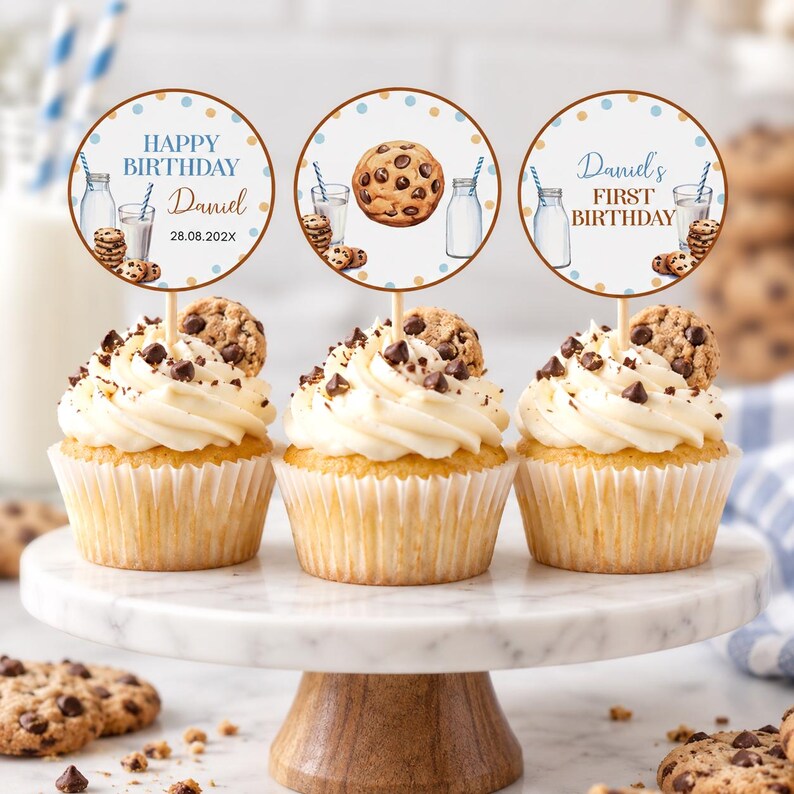 May include: Three cupcakes with white frosting and chocolate chips, each topped with a circular paper topper. The toppers feature illustrations of milk bottles, cookies, and text including Happy Birthday, Daniel, and First Birthday with the date 28.08.202X.