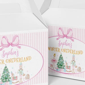 May include: Two white cardboard gable boxes featuring a pink striped border and a central oval frame. The design includes a pink bow, the text "Sophia's WINTER ONEDERLAND," a ballerina, a Christmas tree, a nutcracker, and gift boxes.