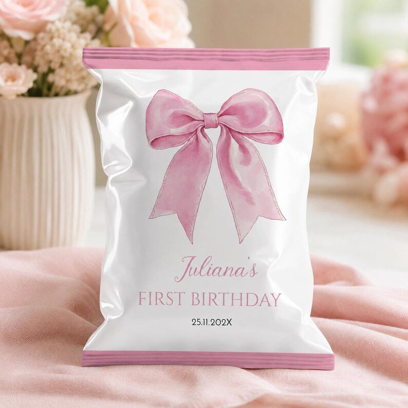 May include: A white snack bag with pink horizontal bands at the top and bottom. The center features a large pink watercolor bow illustration. Text reads: Juliana's FIRST BIRTHDAY 25.11.202X. The bag has a crimped seal design at the edges.