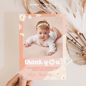 May include: A rectangular thank you card featuring a photo of a baby lying down, framed by a peach-colored border with white daisy illustrations. The text reads: thank you FOR MAKING MY BIRTHDAY SO SWEET AND SPECIAL! Love, Annabella. GOOBER STUDIO PRINTS.