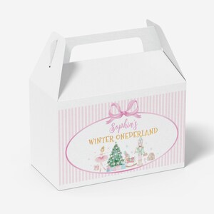 May include: A white gable box featuring a pink and white vertical striped pattern. The front displays an oval frame with a pink bow, containing the text "Sophia's WINTER ONEDERLAND" above illustrations of a Christmas tree, a nutcracker, and a ballerina.