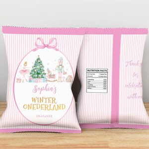 May include: A pink and white striped snack bag featuring a central oval frame with a pink bow. Inside the frame is a Christmas tree, a ballerina, and a nutcracker. Text reads Sophia's WINTER ONEDERLAND 16.12.202X. The back includes a nutrition facts label.