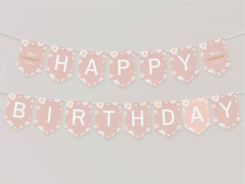 Op de afbeelding: Een tweedelige vlaggenlijn met oudroze vlaggetjes versierd met een wit madeliefjespatroon. De witte letters vormen HAPPY BIRTHDAY. De twee buitenste vlaggetjes bevatten de tekst MILA is turning one! en een datum in een klein wit lettertype.