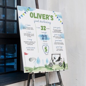 May include: A watercolour-style first birthday sign for a boy named Oliver. The sign features a golf buggy, a golf club, and a tooth with the number 5 on it. The sign also includes information about Oliver's age, height, weight, and favourite foods, songs, books, and toys.
