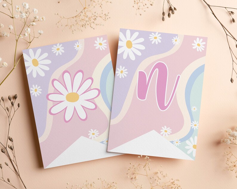 Op de afbeelding: Twee rechthoekige wimpels met een golvende pastelachtergrond van lavendel, roze en lichtblauw. De ene vlag toont een grote witte margriet met een geel hart, terwijl de andere een grote roze kleine letter n bevat.