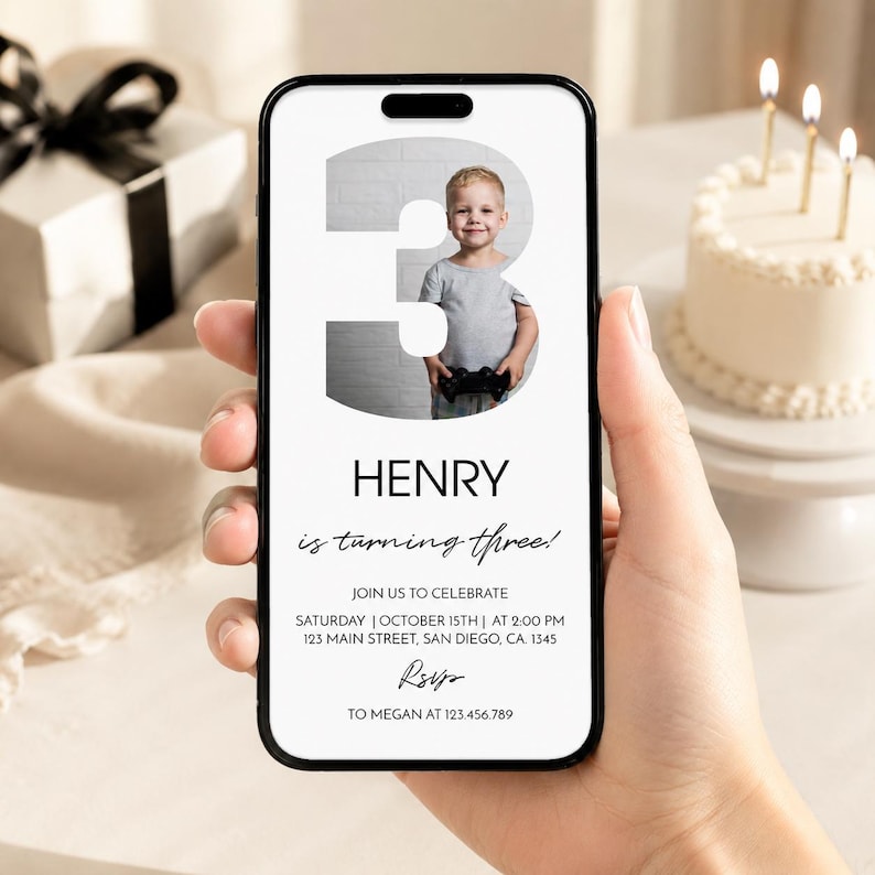 Op de afbeelding: Een digitale verjaardagsuitnodiging op een smartphonescherm met een groot cijfer drie en een foto van een jong kind met een gamecontroller. De tekst luidt Henry is turning three, join us to celebrate, Saturday, October 15th, at 2:00 PM, 123 Main Street, San Diego, CA, 1345, RSVP to Megan at 123.456.789.