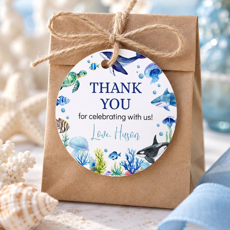 Pu&ograve; includere: Un sacchetto regalo in carta marrone legato con spago e un'etichetta rotonda bianca con illustrazioni ad acquerello di creature marine tra cui una balena, uno squalo, una tartaruga e una medusa. Il testo recita THANK YOU for celebrating with us! Love, Huson.
