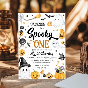 May include: A white Halloween-themed invitation card featuring watercolor illustrations of ghosts, pumpkins, bats, and candy. The text reads: Jackson is a Spooky ONE, Join us to celebrate His 1st Boo-day, Sunday, October 30th, 5:00 PM, 123 Spooky Street, Ohio.