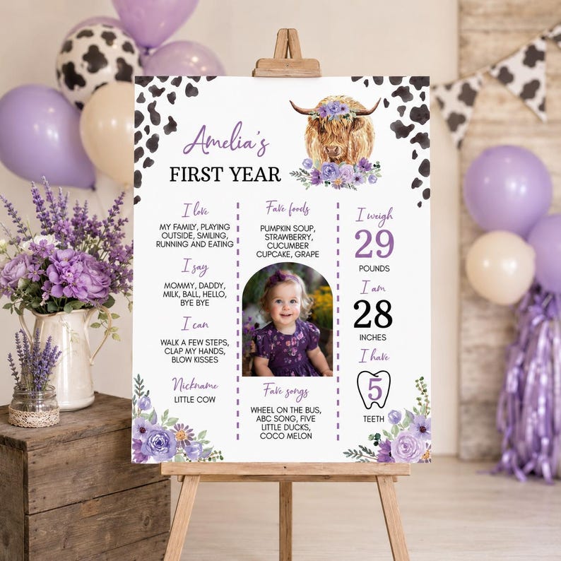 May include: A white milestone birthday sign featuring a watercolor Highland cow with purple flowers, black cow print borders, and text detailing Amelia's first year, including weight of 29 pounds, height of 28 inches, and 5 teeth.