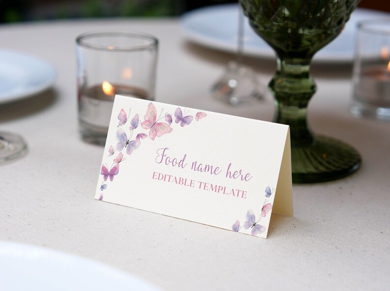 Peut inclure: Une carte pli&eacute;e de couleur cr&egrave;me avec une surface textur&eacute;e orn&eacute;e de papillons de style aquarelle dans des tons roses et violets. Le texte "Food name here" est imprim&eacute; en &eacute;criture cursive au-dessus des mots "EDITABLE TEMPLATE" en majuscules.