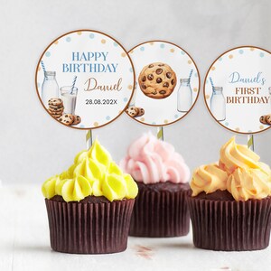 May include: Three cupcakes with yellow, pink, and orange frosting, each topped with a circular paper topper. The toppers feature illustrations of milk bottles, cookies, and text including "HAPPY BIRTHDAY Daniel 28.08.202X" and "Daniel's FIRST BIRTHDAY".