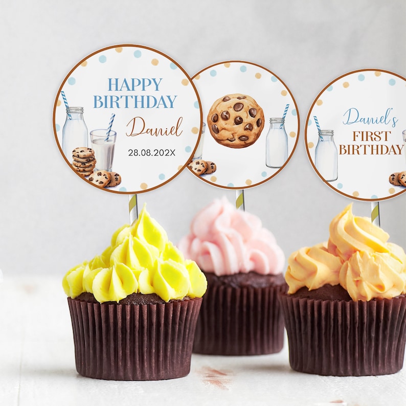 May include: Three cupcakes with yellow, pink, and orange frosting, each topped with a circular paper topper. The toppers feature illustrations of milk bottles, cookies, and text including "HAPPY BIRTHDAY Daniel 28.08.202X" and "Daniel's FIRST BIRTHDAY".