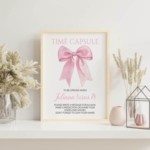 May include: A white frame with a pink bow and the text "TIME CAPSULE" at the top. The text below the bow reads "TO BE OPENED WHEN Juliana turns 18".  The text below that reads "PLEASE WRITE A MESSAGE FOR JULIANA MAKE A PREDICTION OR SHARE YOUR HOPES AND WISHES DON'T FORGET TO SIGN YOUR NAME".