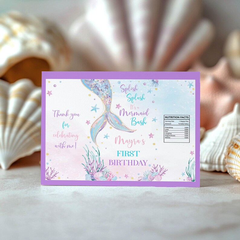 May include: A rectangular card with a purple border featuring a watercolor mermaid tail, starfish, and coral illustrations. Text reads: Splish Splash It's a Mermaid Bash, Mayra's FIRST BIRTHDAY, and Thank you for celebrating with me, plus a nutrition label.