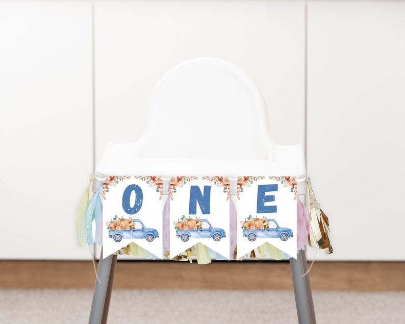 May include: A high chair banner featuring three white pennants with blue letters spelling ONE. Each pennant displays a watercolour illustration of a blue pickup truck carrying orange pumpkins and autumn foliage, accented by colourful hanging tassels.