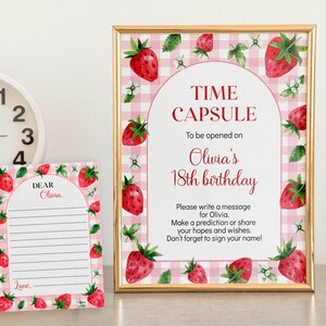 May include: A time capsule sign and a matching message card featuring a pink and white gingham background with watercolor strawberry illustrations. The sign reads: TIME CAPSULE To be opened on Olivia's 18th birthday. Please write a message.