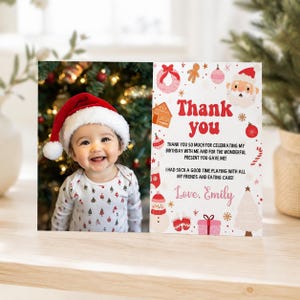 May include: A rectangular thank you card featuring a photo of a smiling baby wearing a red and white Santa hat and a patterned long-sleeve shirt. The right side displays the text Thank you and a message from Emily with festive holiday icons.