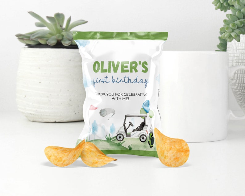 May include: A white chip bag with a green top and a golf-themed design. The bag reads "Oliver's first birthday" and features a golf cart illustration. Three potato chips are in front of the bag.