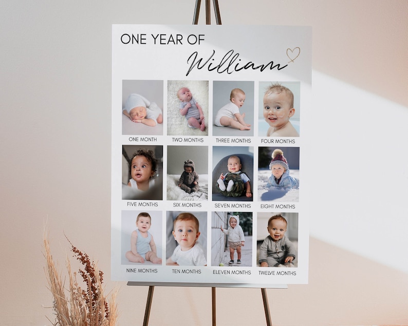 May include: A white rectangular milestone board titled ONE YEAR OF William with a gold heart icon. It features twelve individual photographs of a baby arranged in a grid, each labelled with the corresponding age from one month to twelve months.