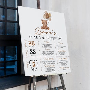 Puede incluir: Un cartel de cumplea&ntilde;os rectangular blanco con una ilustraci&oacute;n de un oso de peluche marr&oacute;n con globos, el texto Liam's BEAR-Y 1ST BIRTHDAY y detalles que incluyen 28 pounds, 32 inches, 5 dientes, comidas, canciones, libros y apodos favoritos.
