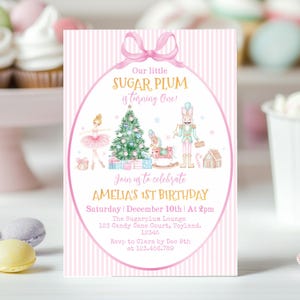 May include: A rectangular birthday invitation card with a pink and white striped background. It features a pink bow at the top, a ballerina, a Christmas tree, a nutcracker, and a rocking horse. Text reads: Our little SUGAR PLUM is turning One! AMELIA'S 1ST BIRTHDAY, Saturday | December 10th | At 2pm, The Sugarplum Lounge, 123 Candy Cane Court, Toyland, 12345, Rsvp to Clara by Dec 8th at 123.456.789.