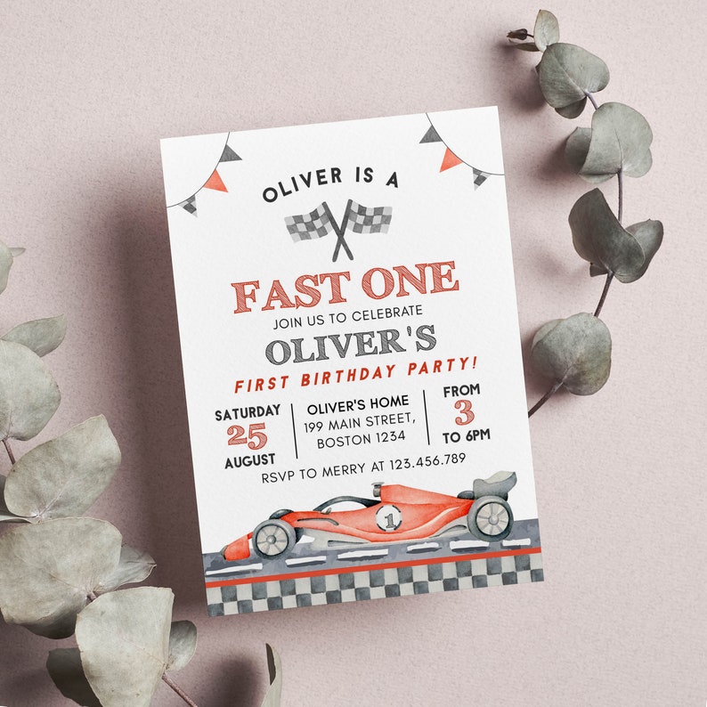May include: A white invitation card with the text "OLIVER IS A FAST ONE" and "OLIVER'S FIRST BIRTHDAY PARTY!". It features a red race car illustration and checkered flag accents. The date and time are also included.