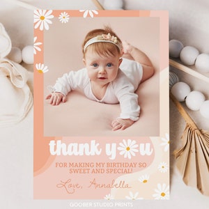 May include: A rectangular thank you card featuring a photo of a baby wearing a floral headband. The card has a peach-colored background with white daisy illustrations and the text: thank you FOR MAKING MY BIRTHDAY SO SWEET AND SPECIAL! Love, Annabella.