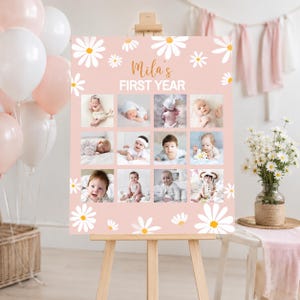 May include: A pink milestone board featuring white daisy illustrations and the text Mila's FIRST YEAR. The board displays a grid of twelve photographs of an infant at different stages, set on a wooden easel with balloons and flowers nearby.