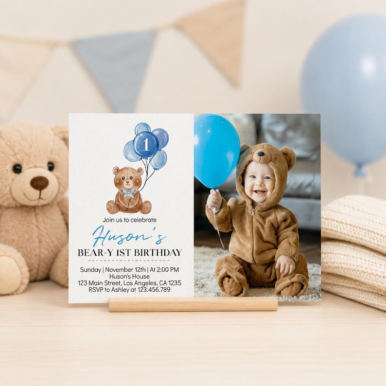 Op de afbeelding: Een rechthoekige verjaardagsuitnodigingskaart met een aquarelillustratie van een bruine teddybeer die blauwe ballonnen met het cijfer &eacute;&eacute;n vasthoudt. De tekst luidt Huson's BEAR-Y 1ST BIRTHDAY, Sunday, November 12th, at 2:00 PM, Huson's House, 123 Main Street, Los Angeles, CA 1235, RSVP to Ashley at 123.456.789. Rechts staat een foto van een kind in een berenkostuum met een blauwe ballon.