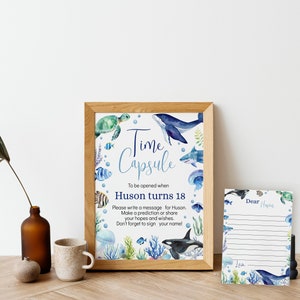 Pu&ograve; includere: Un cartello incorniciato con illustrazioni ad acquerello di vita marina e il testo Time Capsule To be opened when Huson turns 18. Accanto si trova un biglietto a righe abbinato con il testo Dear Huson e Love, decorato con motivi oceanici blu e verdi.