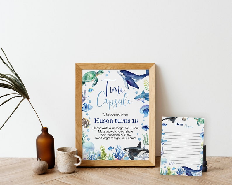Pu&ograve; includere: Un cartello incorniciato con illustrazioni ad acquerello di vita marina e il testo Time Capsule To be opened when Huson turns 18. Accanto si trova un biglietto a righe abbinato con il testo Dear Huson e Love, decorato con motivi oceanici blu e verdi.