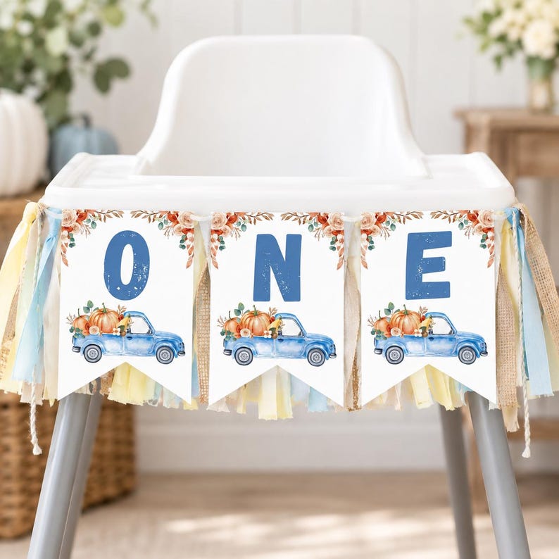 May include: A high chair banner featuring three white triangular pennants with blue letters spelling ONE. Each pennant displays a watercolour illustration of a blue pickup truck carrying orange pumpkins and autumn foliage, accented with fabric tassels.