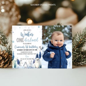 May include: A rectangular birthday invitation card featuring a Winter ONEderland theme with blue snowflakes, arctic animals, and text reading Join us in a Winter ONEderland to celebrate Cameron's 1st birthday, plus a photo of a child in a blue coat.