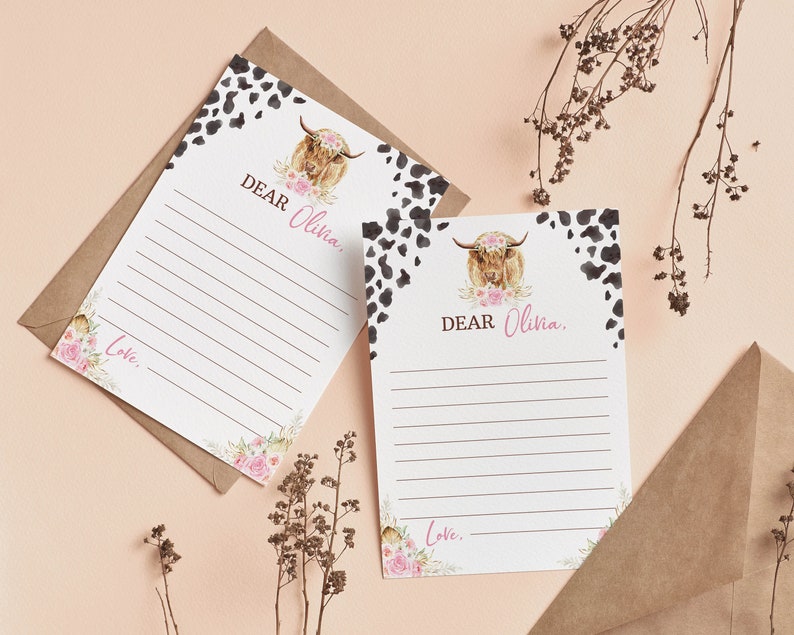 May include: Two blank white cards with black and white cowhide print borders. Each card features a watercolor illustration of a Highland cow with pink flowers. The text "DEAR Olivia." is printed on each card. The cards are on a light brown background.