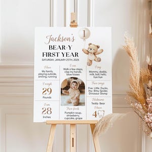 May include: A brown and white first birthday milestone poster with a teddy bear illustration. The poster includes the child's name, Jackson, and details about their first year, including their weight, height, favorite foods, and songs. The poster is decorated with a brown and white color scheme and features a cute teddy bear illustration.