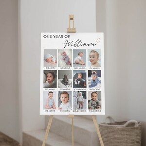 May include: A white rectangular milestone poster titled ONE YEAR OF William with a small heart icon. The poster features twelve individual photographs of a child arranged in a grid, each labelled with a month from one to twelve months below.