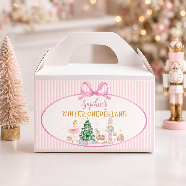 May include: A white gable box with a light pink vertical striped pattern. The front features a pink oval frame with a bow, containing the text Sophia's WINTER ONEDERLAND, a ballerina, a Christmas tree, a rocking horse, and a nutcracker figure.