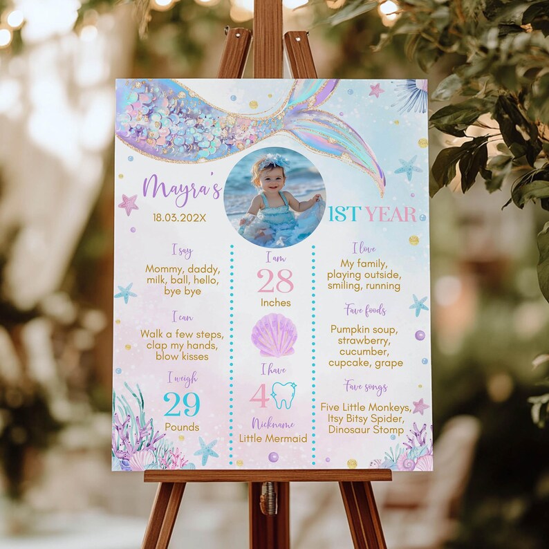 May include: A mermaid-themed first birthday milestone poster with a photo of a baby girl. The poster features a mermaid tail with iridescent scales, a seashell, and a starfish. The poster includes the baby's name, Mayra, and details about her first year, including her height, weight, and favorite foods and songs.