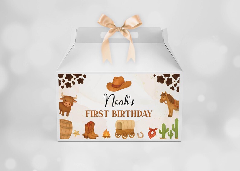 Puede incluir: Una caja blanca con un lazo de sat&eacute;n beige en la parte superior. El frente presenta una ilustraci&oacute;n de tem&aacute;tica western con un sombrero de vaquero marr&oacute;n, un toro, un caballo, un barril, botas, una fogata, una carreta, un cactus y el texto Noah's FIRST BIRTHDAY.