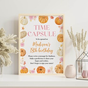 Puede incluir: Un letrero rectangular en un marco de madera clara con el texto TIME CAPSULE To be opened on Madison's 18th birthday. Please write a message for Madison. Make a prediction or share your hopes and wishes. Don't forget to sign your name! Decorado con calabazas y flores rosas en acuarela.