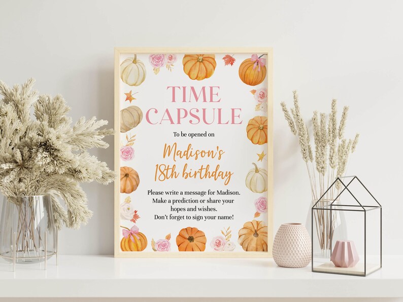 Puede incluir: Un letrero rectangular en un marco de madera clara con el texto TIME CAPSULE To be opened on Madison's 18th birthday. Please write a message for Madison. Make a prediction or share your hopes and wishes. Don't forget to sign your name! Decorado con calabazas y flores rosas en acuarela.