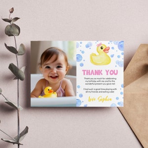 May include: A rectangular thank you card featuring a photo of a child in a bathtub with a yellow rubber duck. The right side displays a watercolor yellow rubber duck with a pink bow, blue bubbles, and the text: THANK YOU, Thank you so much for celebrating my birthday with me and for the wonderful present you gave me! I had such a good time playing with all my friends and eating cake! Love, Sophia.