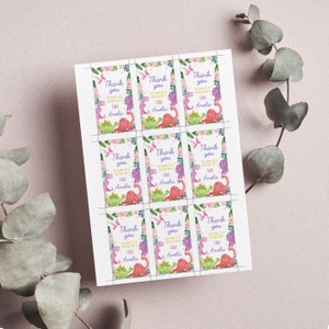 K&ouml;nnte beinhalten: Ein Bogen mit neun rechteckigen Geschenkanh&auml;ngern aus Papier mit einem Aquarell-Design aus Dinosauriern und Blumen. Jeder Anh&auml;nger enth&auml;lt den Text Thank you for coming to my birthday party Love Amelia in violetter Schrift, umgeben von gr&uuml;nen Bl&auml;ttern.